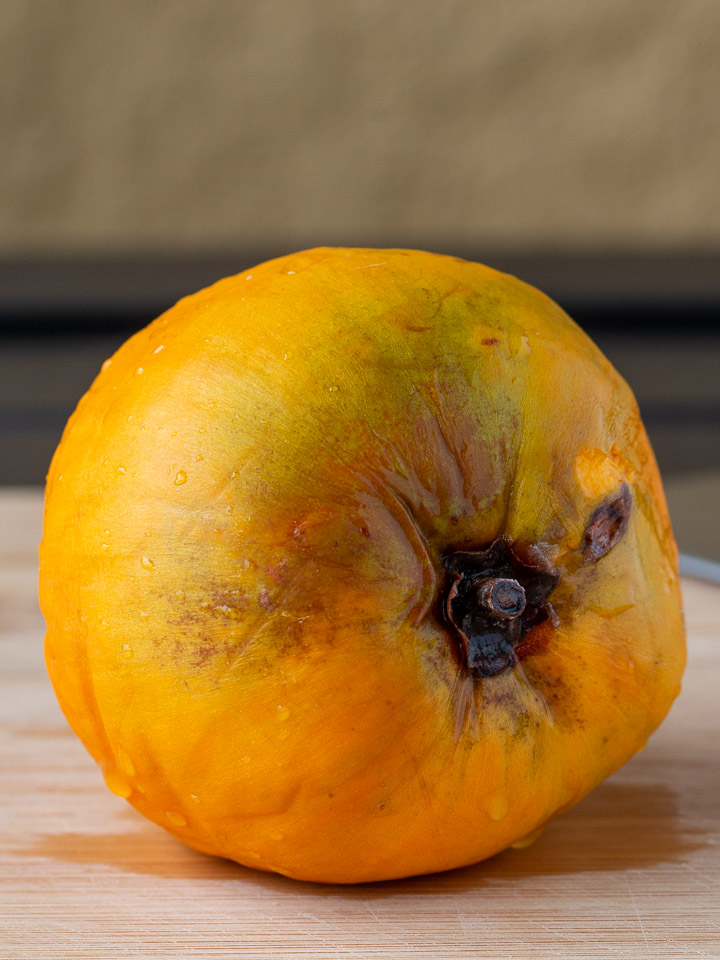 Whole bright yellow orange canistel sitting on a cutting board.