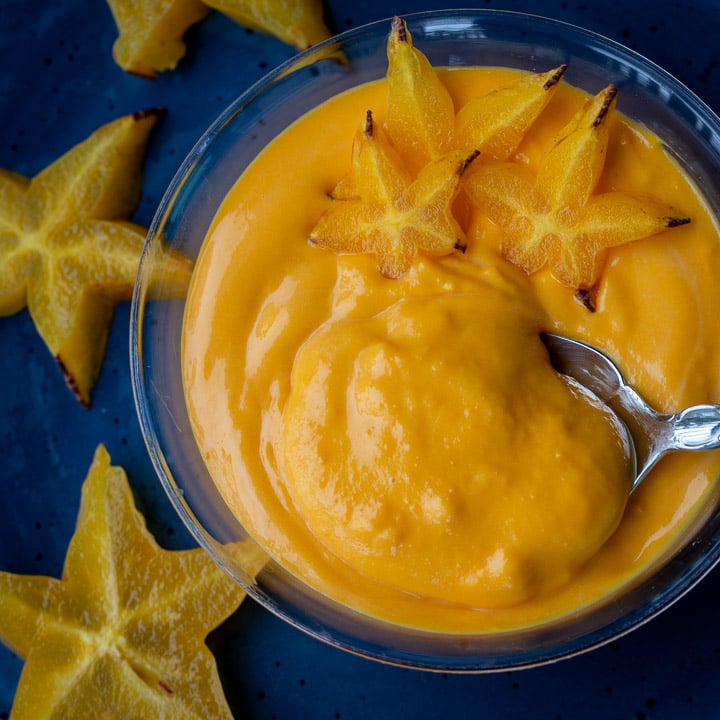 Creamy egg fruit dessert soup in a blue bowl topped with star fruit with a spoon scooping out a bite.