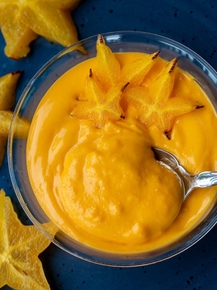 Creamy egg fruit dessert soup in a blue bowl topped with star fruit with a spoon scooping out a bite.
