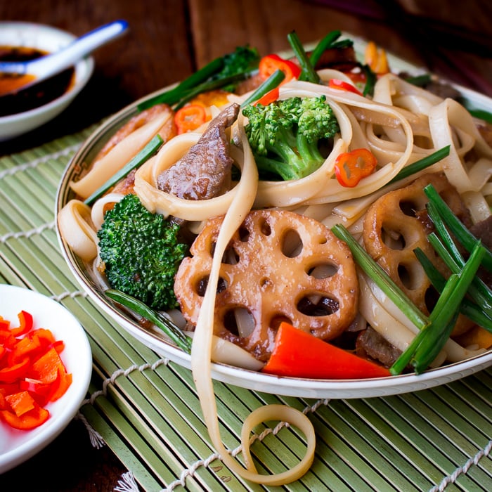 Spicy Beef and Longevity Noodles with lotus root on a green mat.