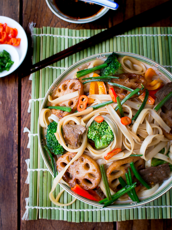 Spicy Beef and Longevity Noodles  on a green mat with chop sticks and extra garnishes.