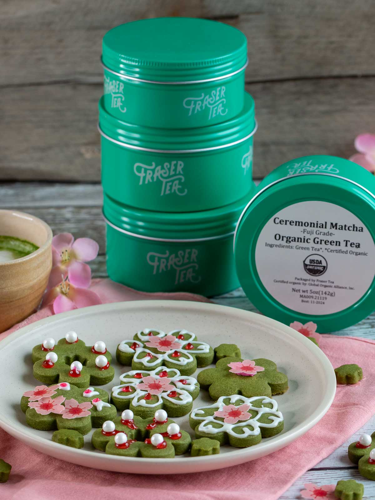Sakura Shortbread Matcha cookies on a white plate with tins of matcha in the background.