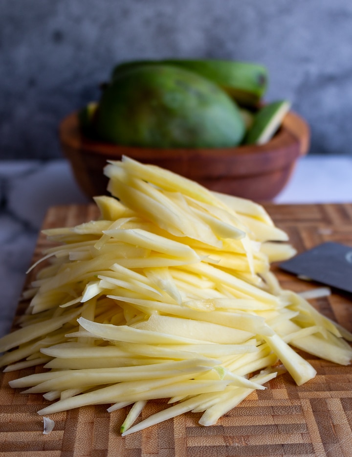 Julienned sliced green mango on a wooden cutting board.