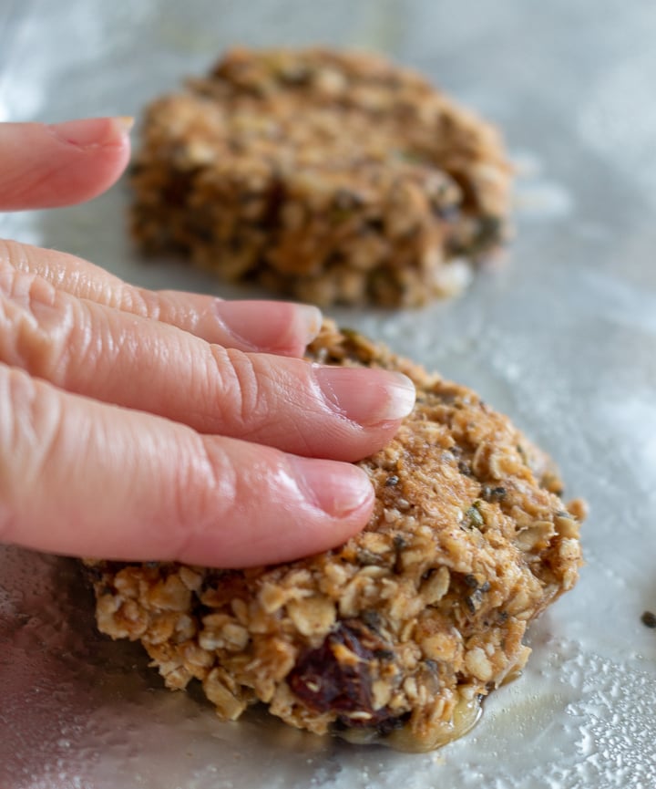 Unbaked cookies on cookie tray getting formed into round disks with fingers.