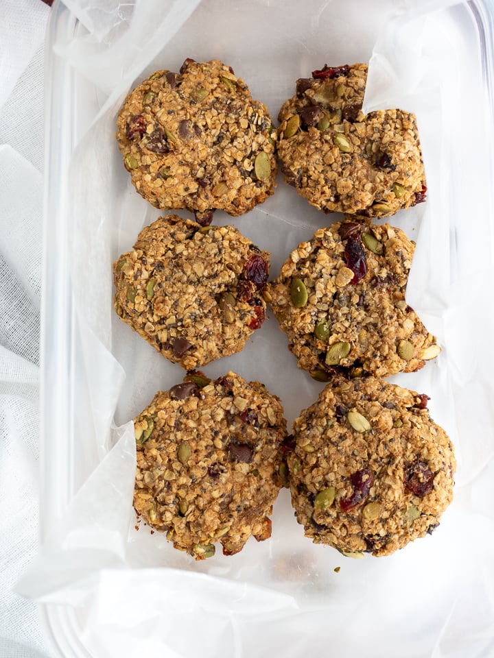 Showing baked and cooled cranberry Oatmeal Breakfast cookies in a freezer safe sealed container lined with layers of parchment paper between each to prevent sticking. 