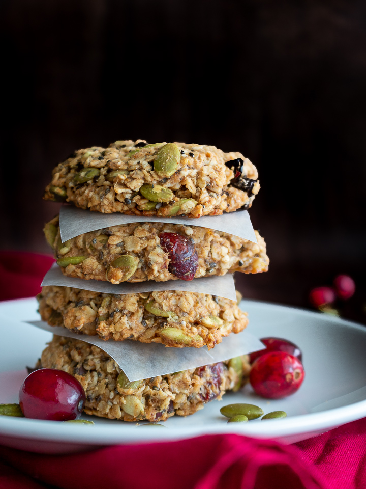 4 delicious breakfast cookies stacked on top of eachther with parchment paper in between on a white plate with cranberries on plate.