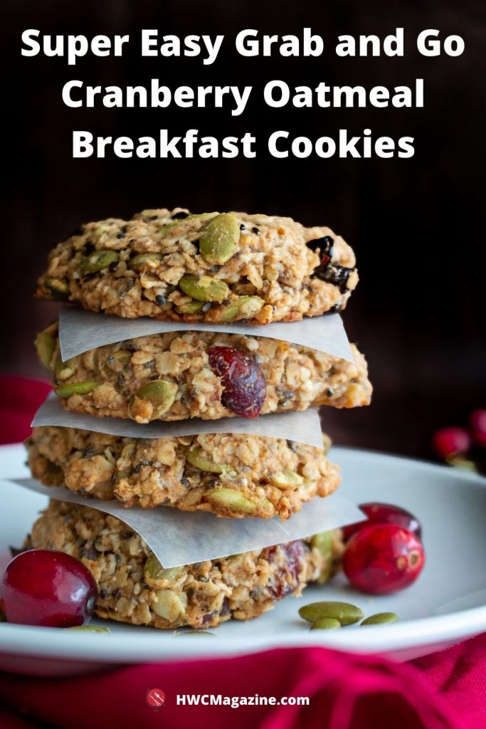 4 Cranberry Oatmeal Breakfast Cookies stacked on top of each other with parchment paper between each and extra cranberries on side on a white flat dish.
