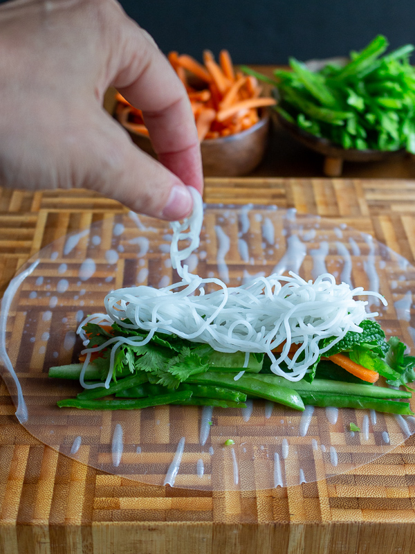 Adding rice vermicelli noodles on top of vegetables and fresh herbs.