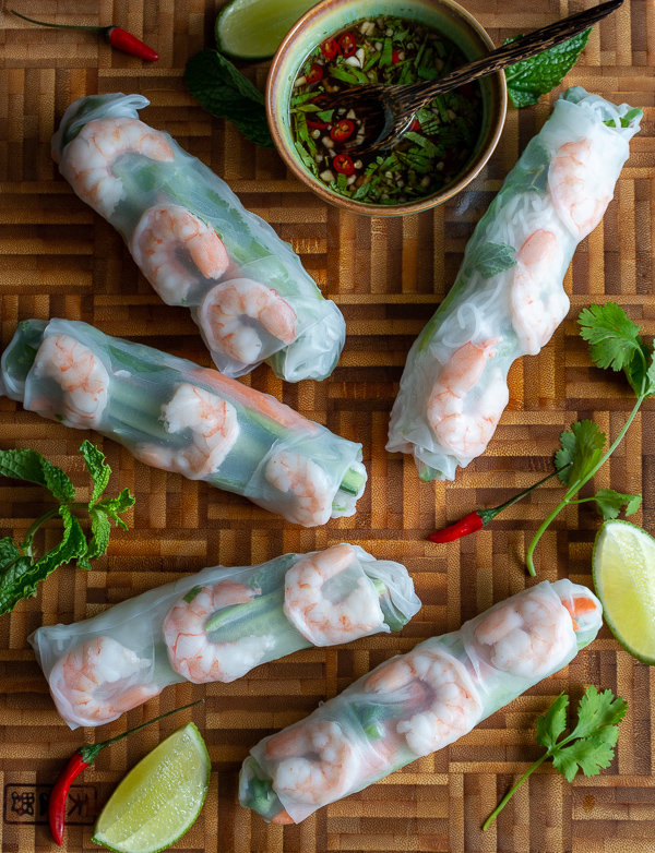 5 summer rolls with sauce and garnishes on a wooden board. 