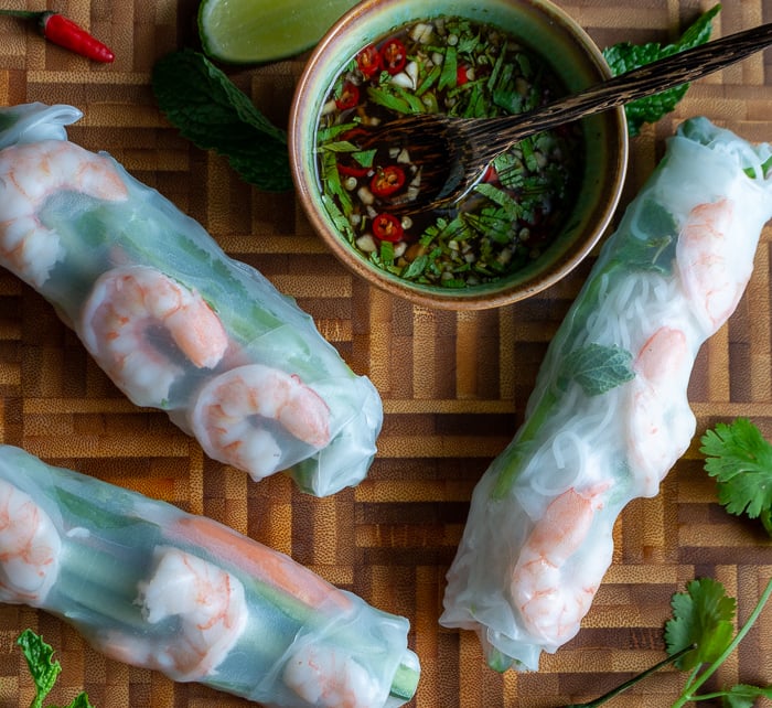 Three summer rolls on a wooden blackboard with a small bowl of dipping sauce.