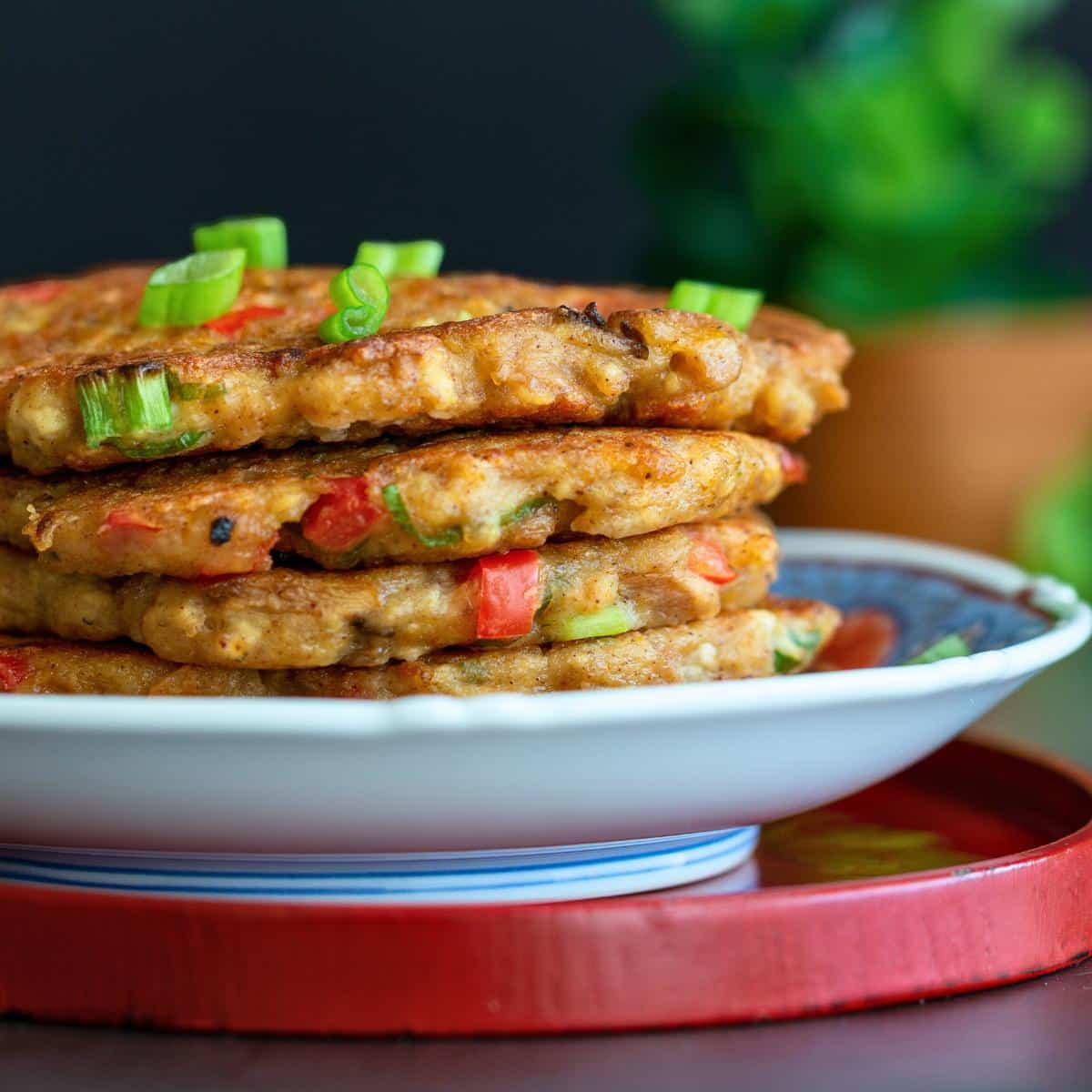 4 vegetable pancakes stacked on a blue and white Chinese plate, garnished with scallions. 