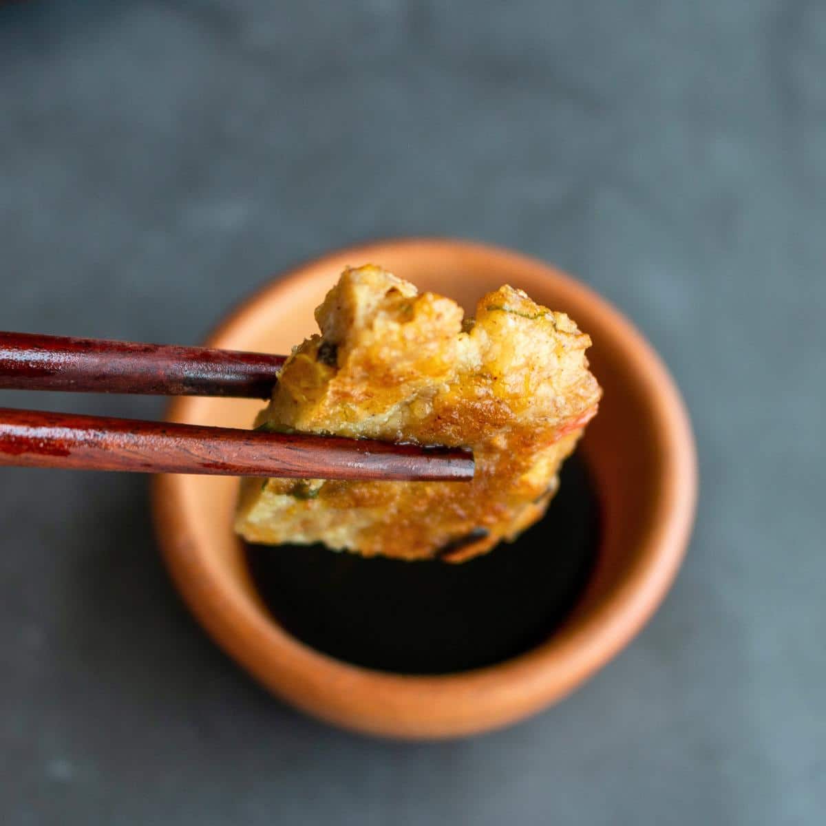 A wedge of Chinese pancake getting held with wooden chopsticks and dipped into sauce. 