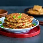 A stack of savory Asian tofu vegetable pancakes on a blue and white plate on a red serving platter.