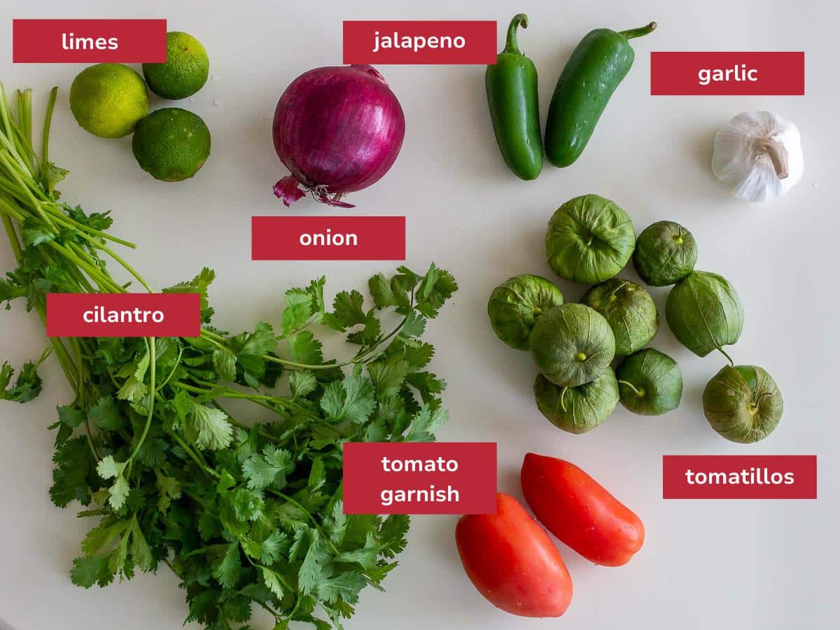 Ingredients to make green tomatillo verde salsa laid out on a beige table.