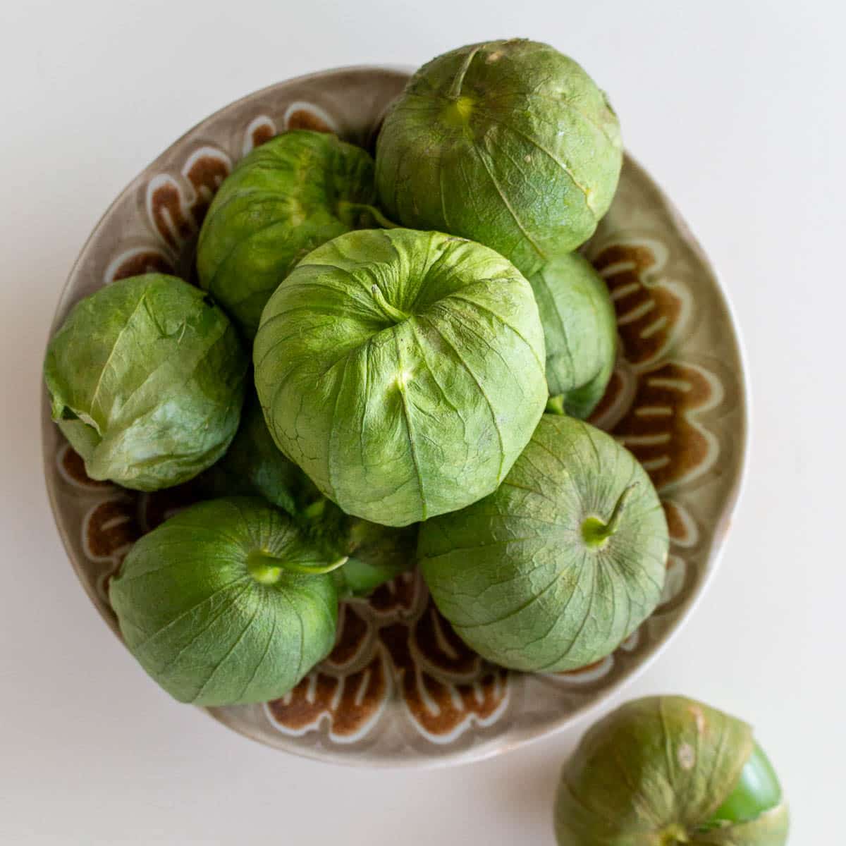 Fresh green tomatillos with their skin on in a brown bowl. 