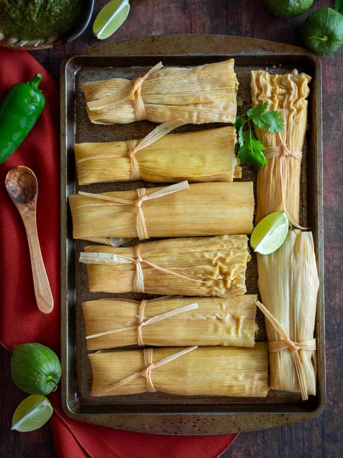 Gluten free Vegetarian tamale verde laid out on a flat square plate with extra tomatillo salsa on the side. 