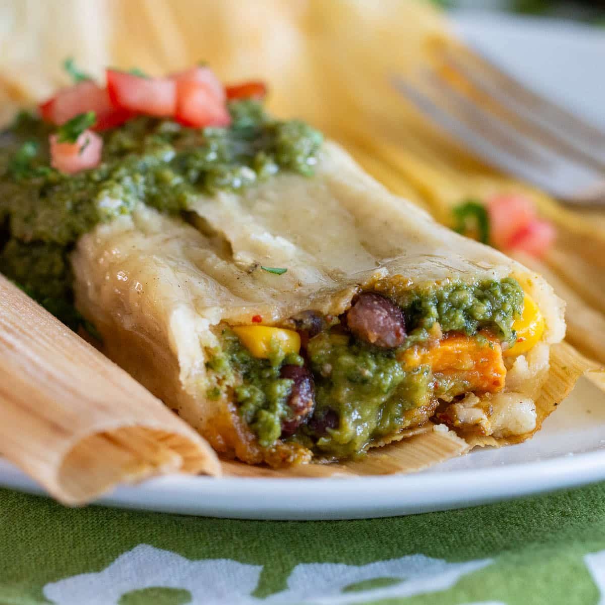 A vegetarian tamale freshly steamed and opened up to show the roasted vegetables and the verde salsa. 