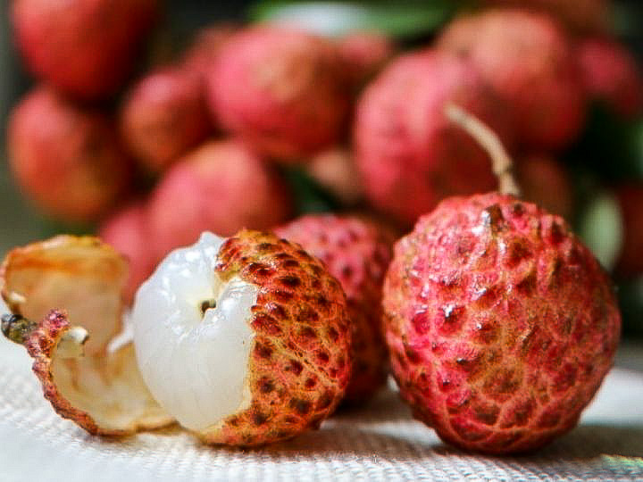 Fresh lychees with one peeled showing the white flesh.