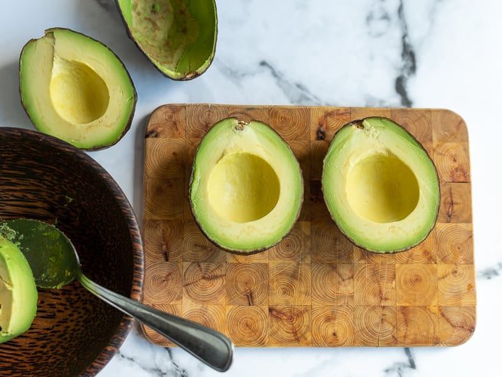 Avocados cut in half on a cutting board. 