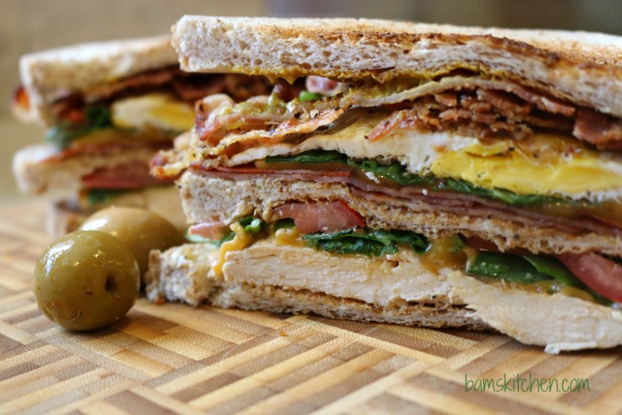 Triple Decker Sammie cut in half showing all the layers and additions with a couple of olives on the side.