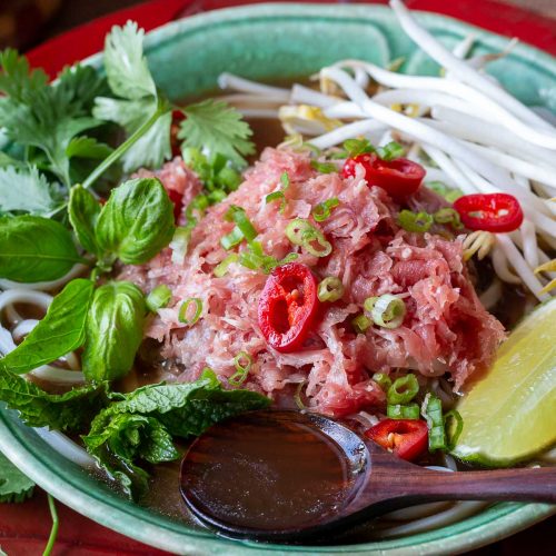 Quick beef pho in a green bowl with a spoonful of soup and lots of fresh herbs.