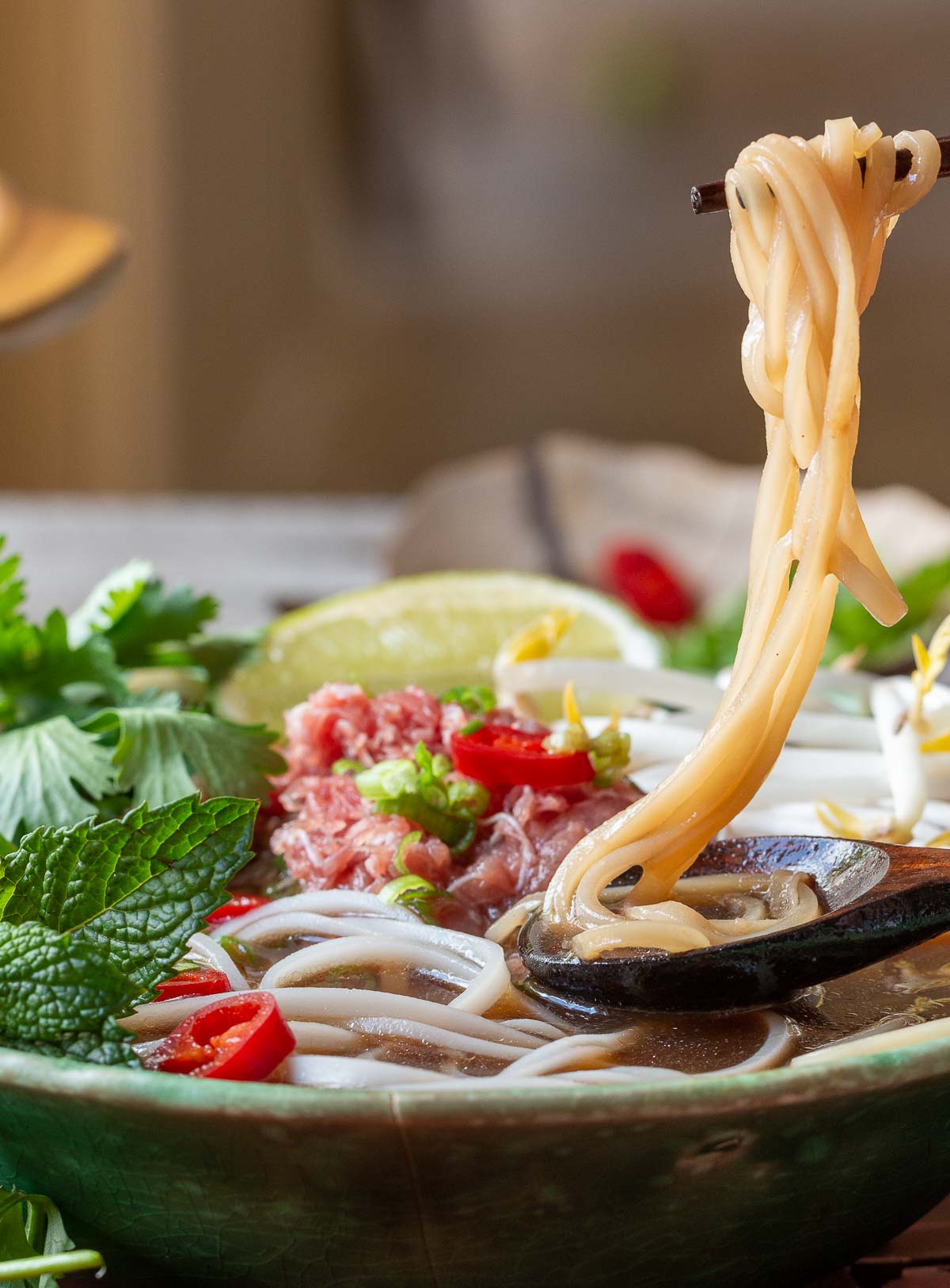 Gluten free rice noodles in chopsticks with a spoonful of broth underneath.