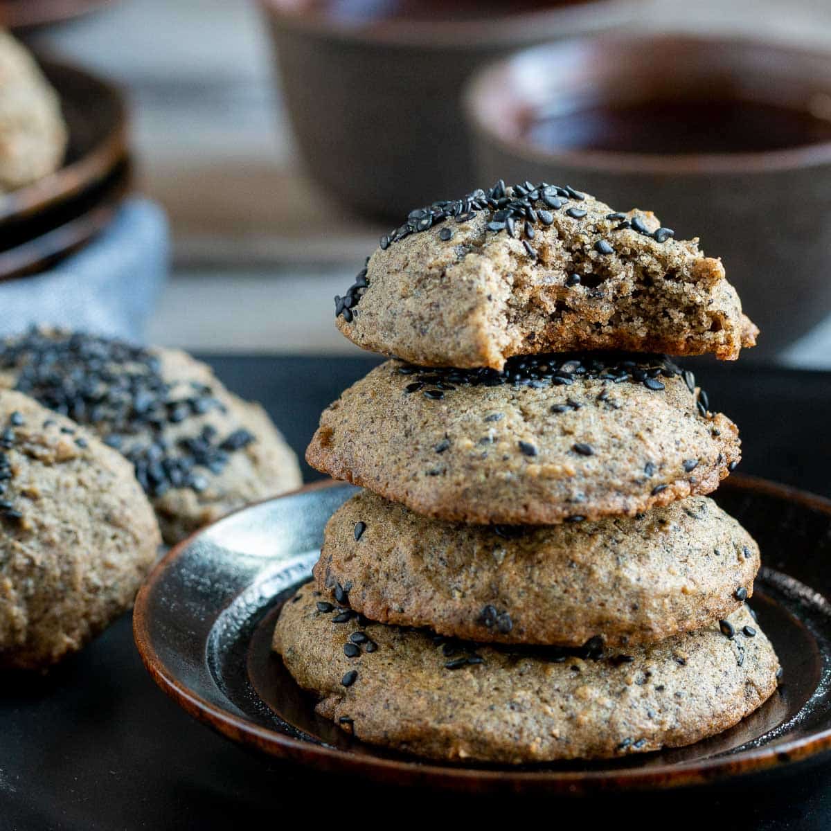 One black sesame cookie with a bite out of it on a stack of cookies.
