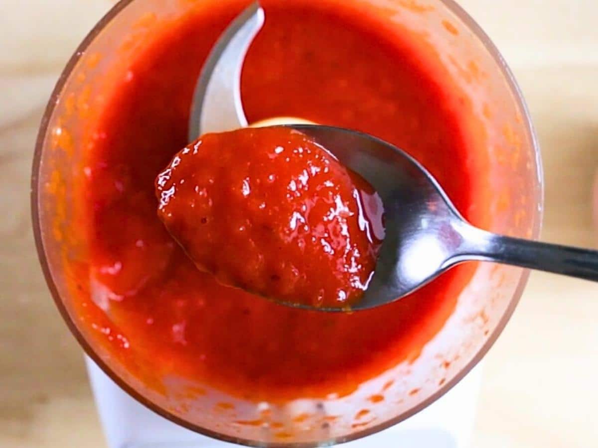 Homemade paprika cream in a food processor with a spoonful showing the rich red paste. 