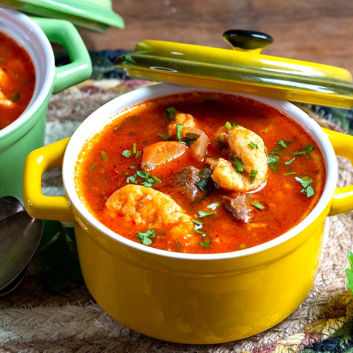 A heart bowl of Hungarian Goulash Soup in a yellow bowl with petite dumplings and garnished with parsley.