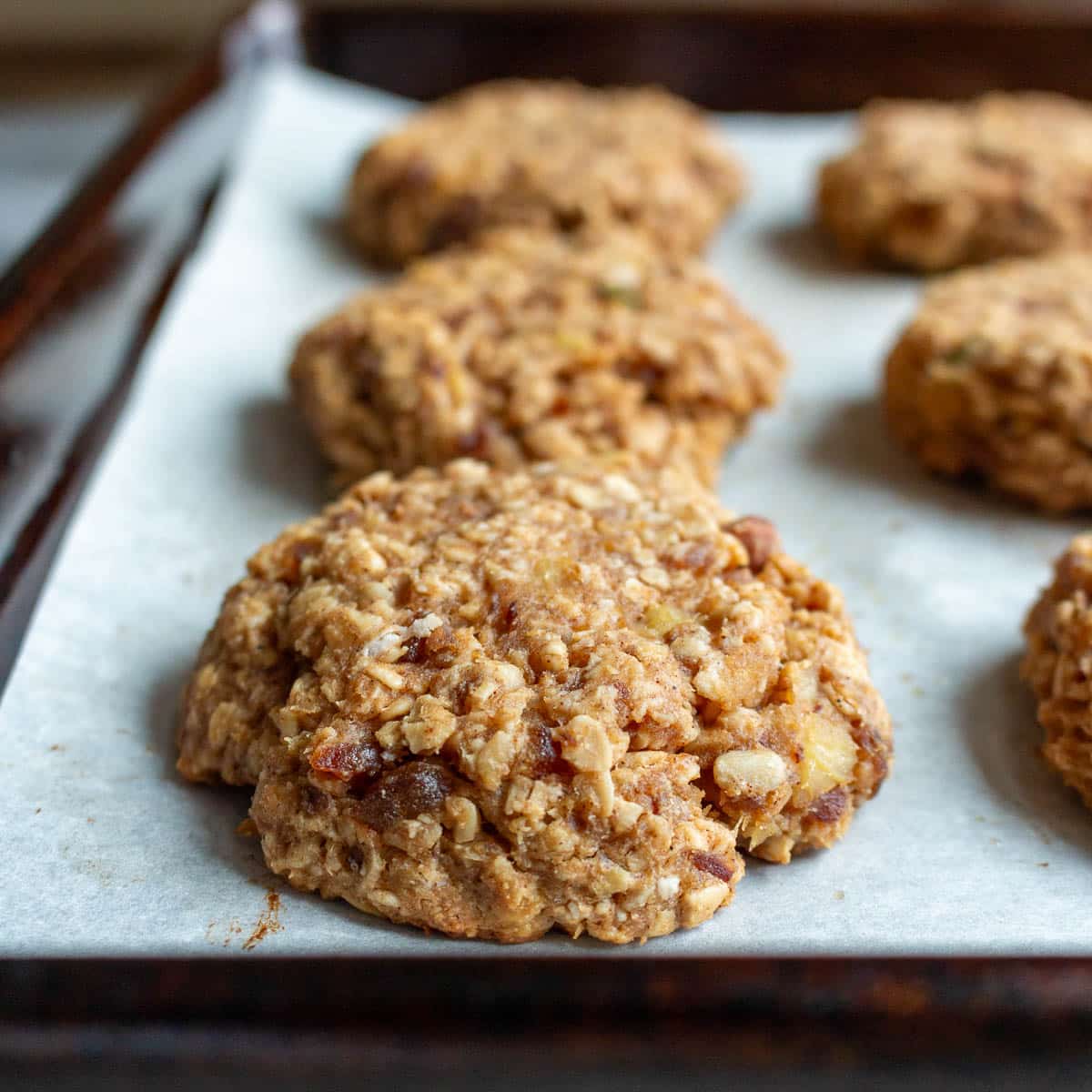 Baked oat cookies with dates resting on the cookie sheet after baking.