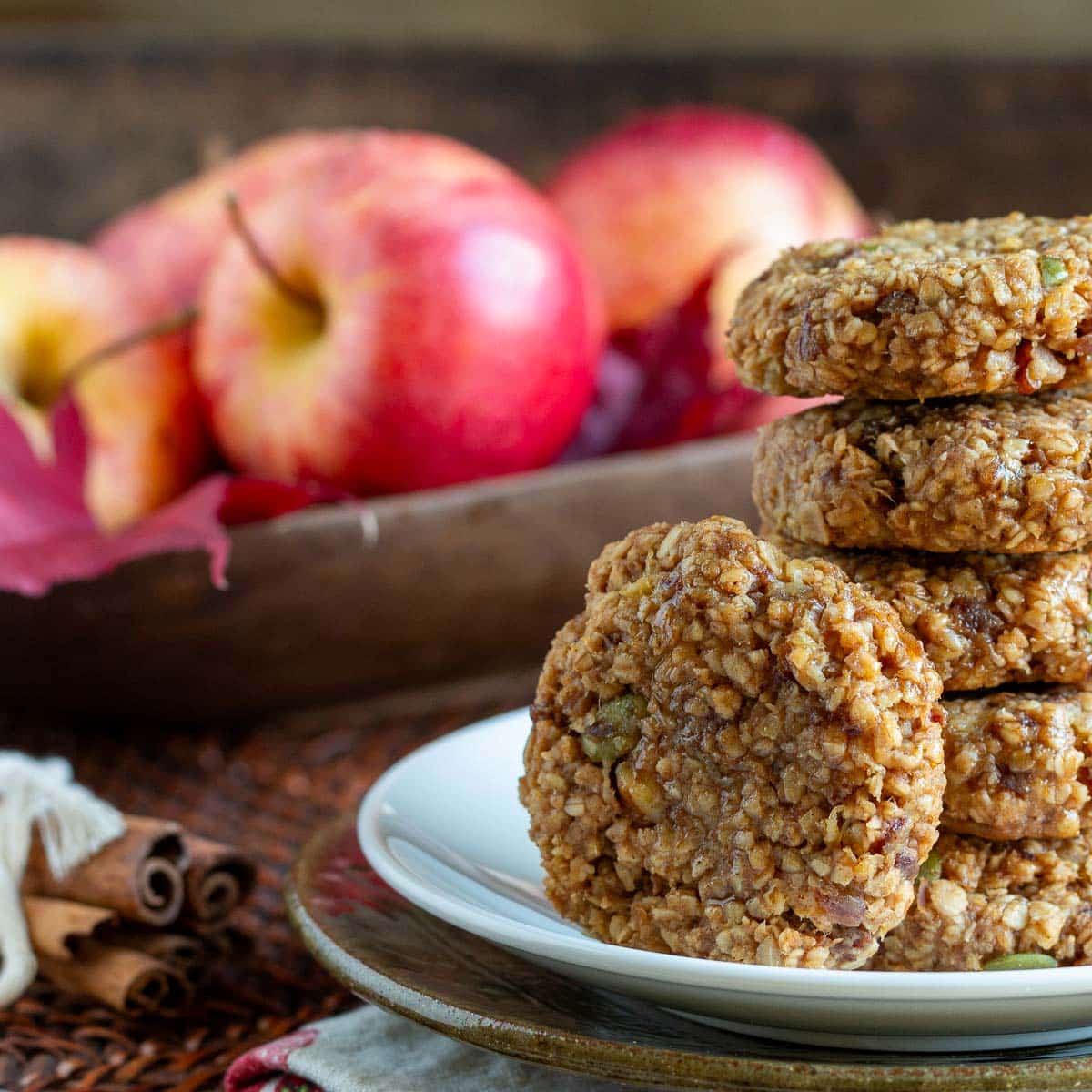 Apple pie breakfast cookies stacked on a white plate with red gala apples in the background.