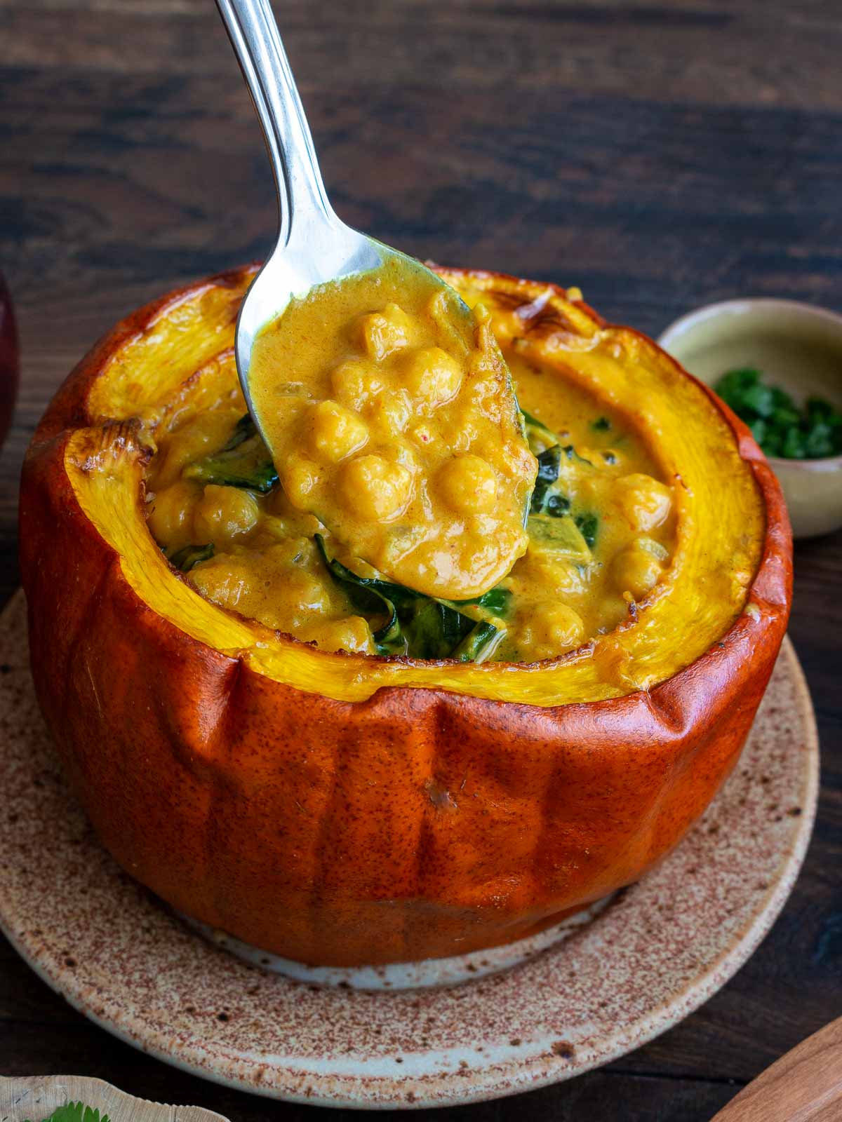 The bite shot of delicious coconut chickpea curry in a spoon inside the edible pumpkin bowl.