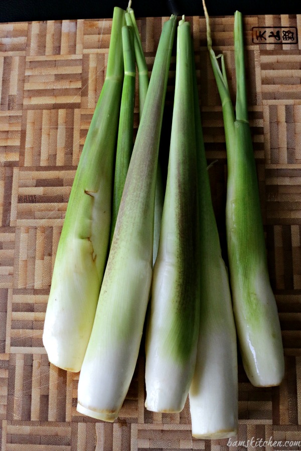 Wild rice stems raw and whole on a bamboo cutting board.