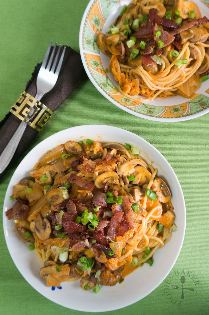 2 plates of Creamy Kimchi Pasta topped with bacon on a green napkin.