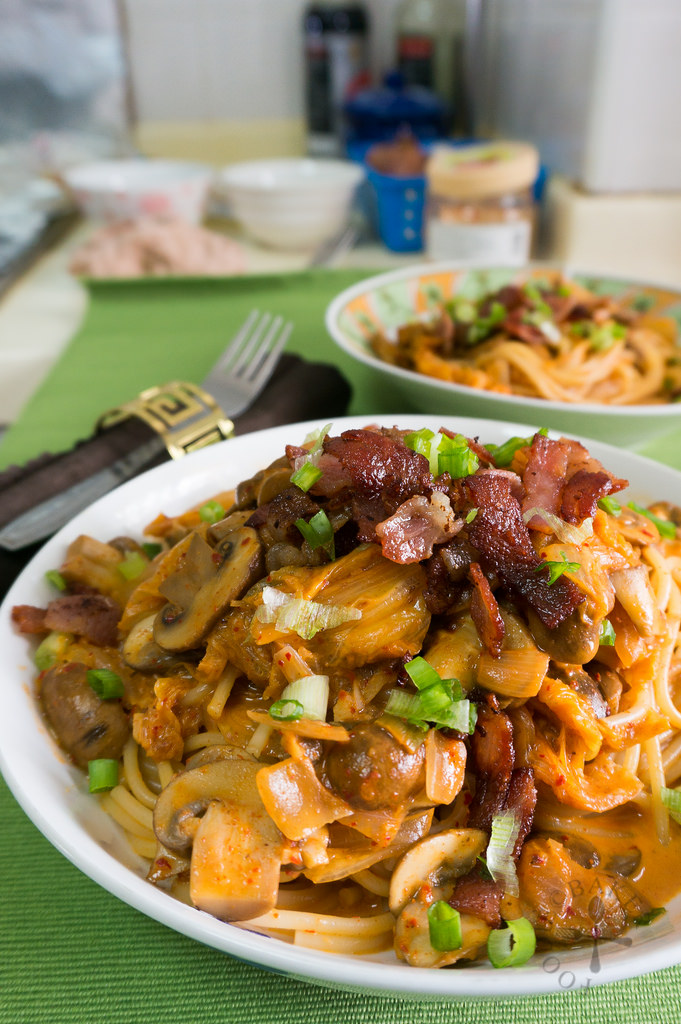 Creamy Kimchi Pasta in a white bowl with tons of mushrooms and bacon and creamy sauce.
