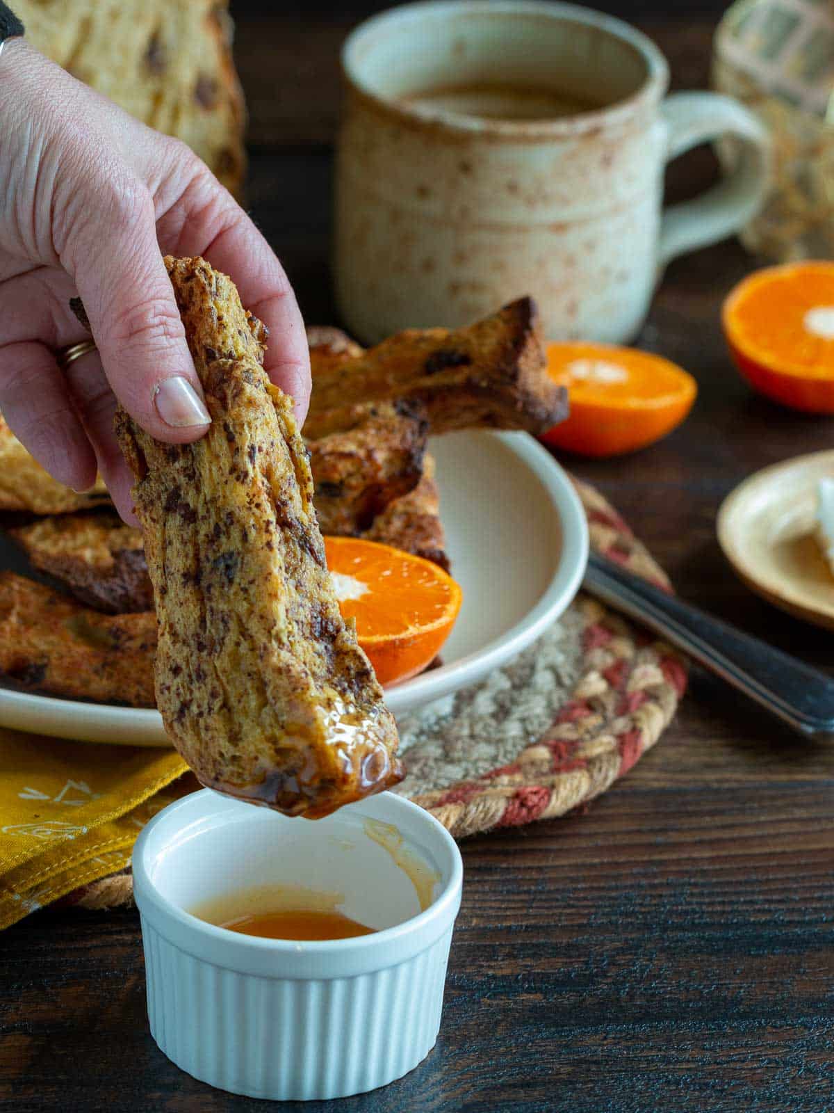 Panettone French toast stick getting dipped into the maple bourbon syrup.