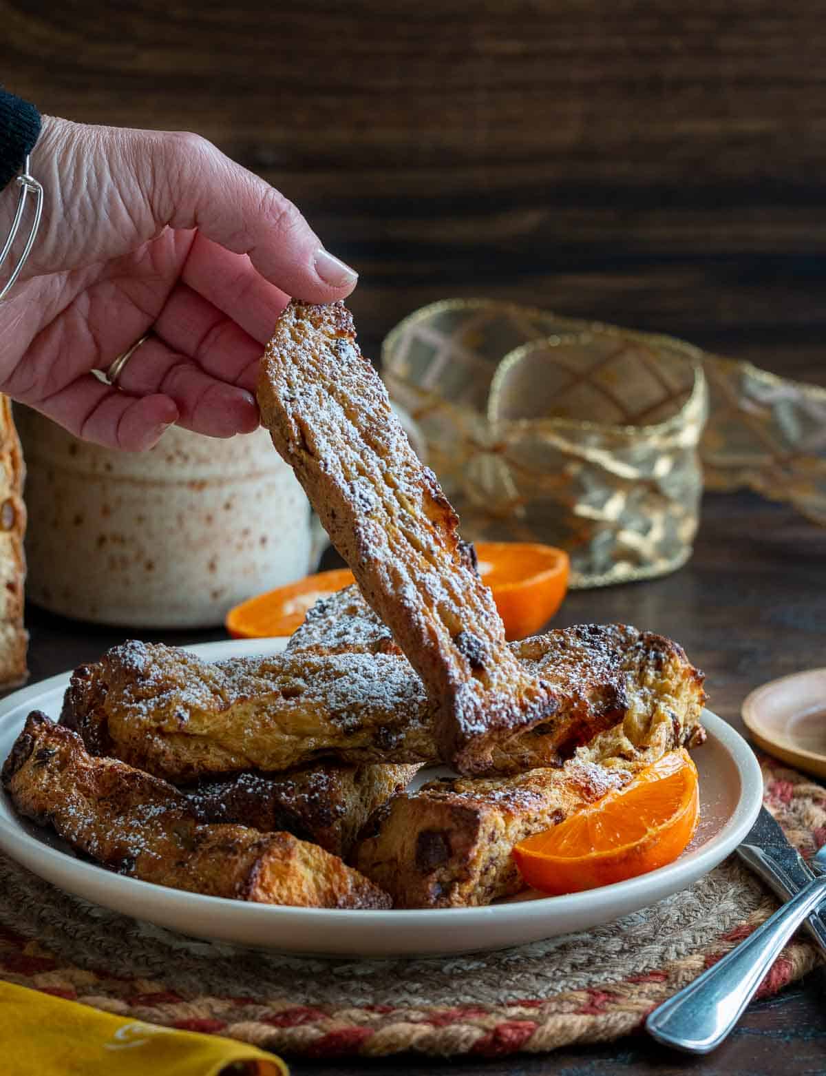 Holding a toasted French toast stick dusted with powdered sugar.