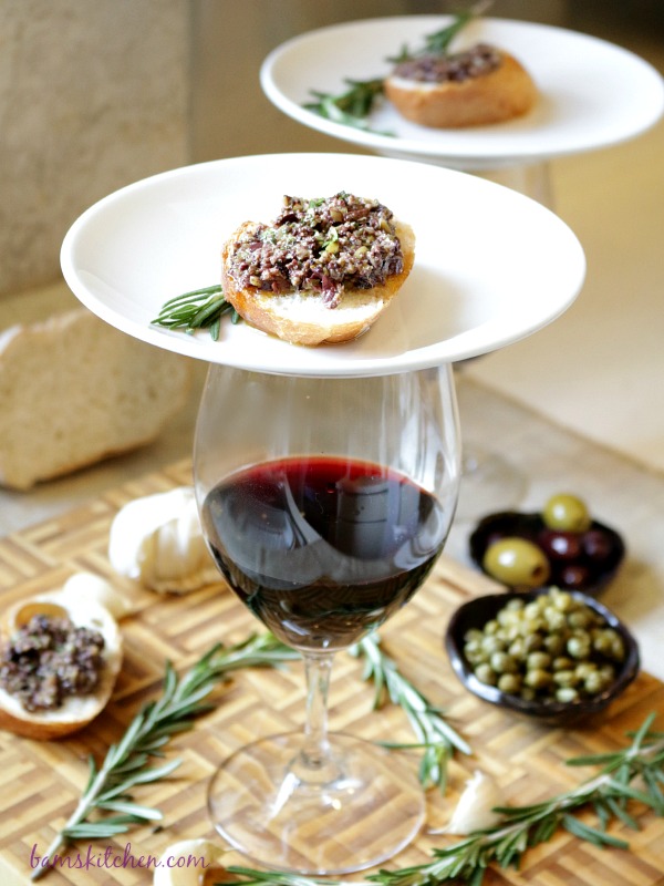 Crostini on a white plate balancing over a glass of red wine. 