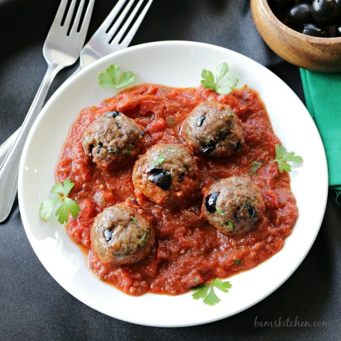 5 meatballs nestled in a bowl of tomato wine sauce.