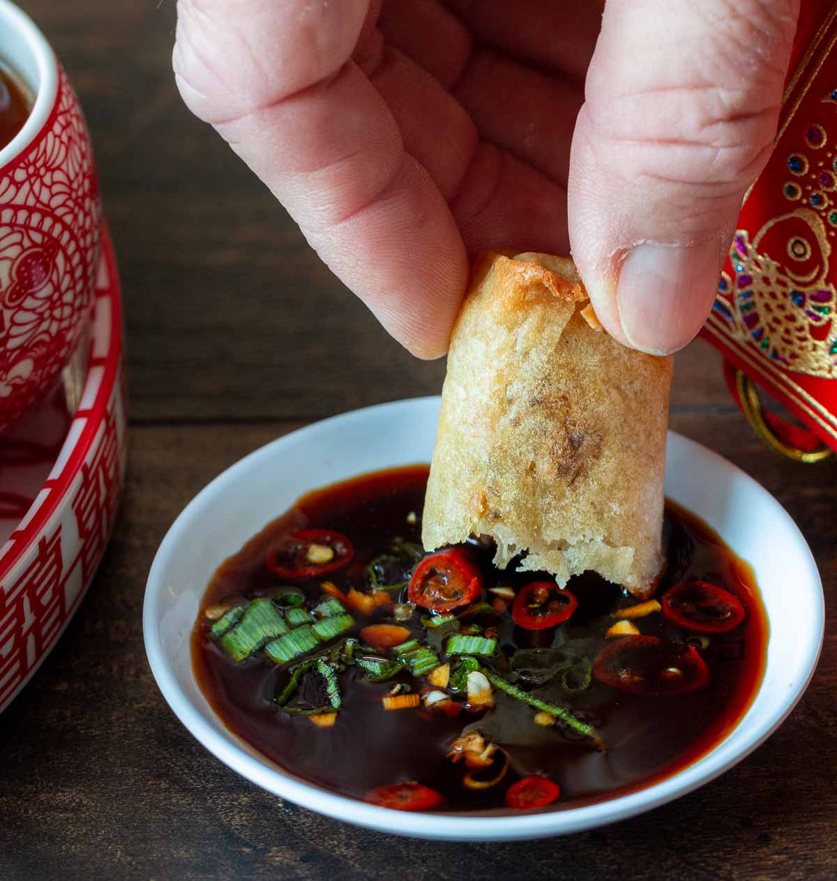 Spring roll getting dunked into spicy dipping sauce.