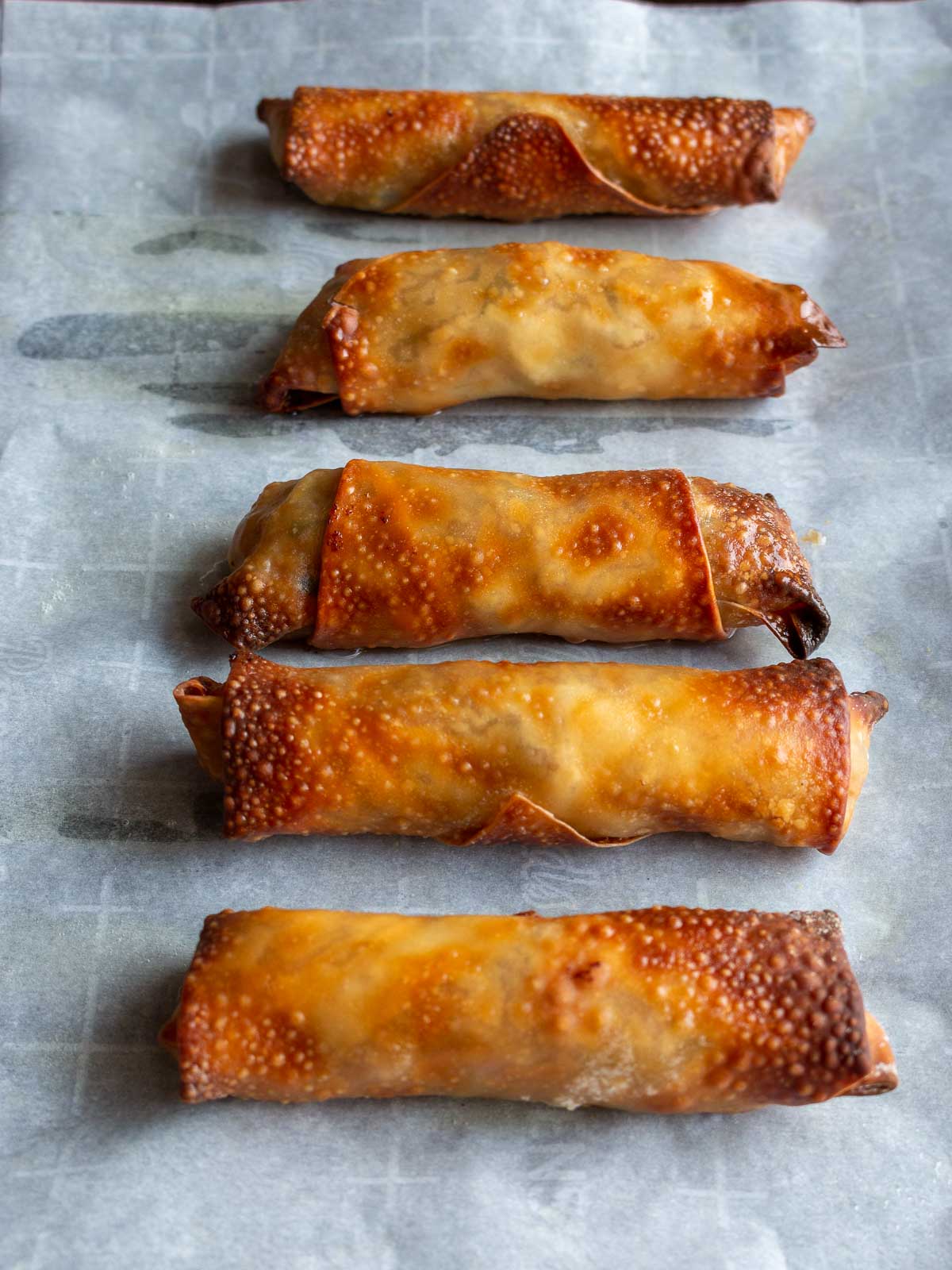 Spring rolls hot out of the air fryer on a lined tray.