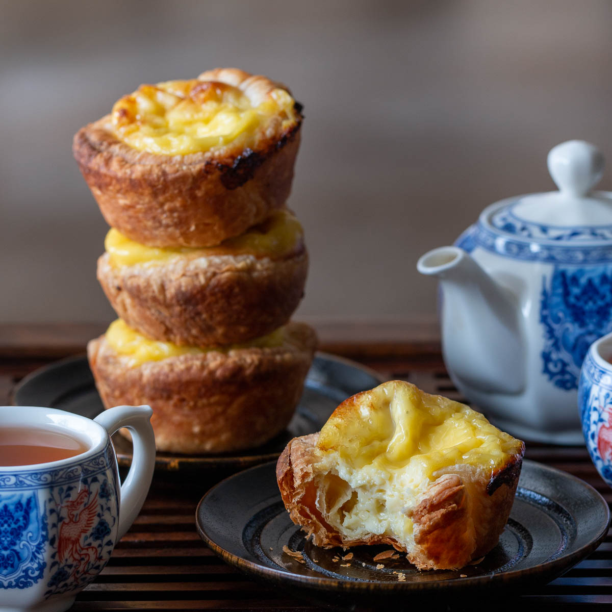 Hong Kong egg tarts stacked on top of each other with a blue tea pot and tea cups.