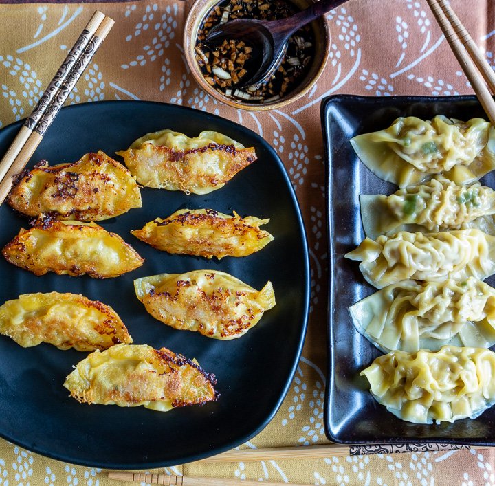 Jiaozi Chinese pot stickers and boiled dumplings on black plates with dipping sauce.