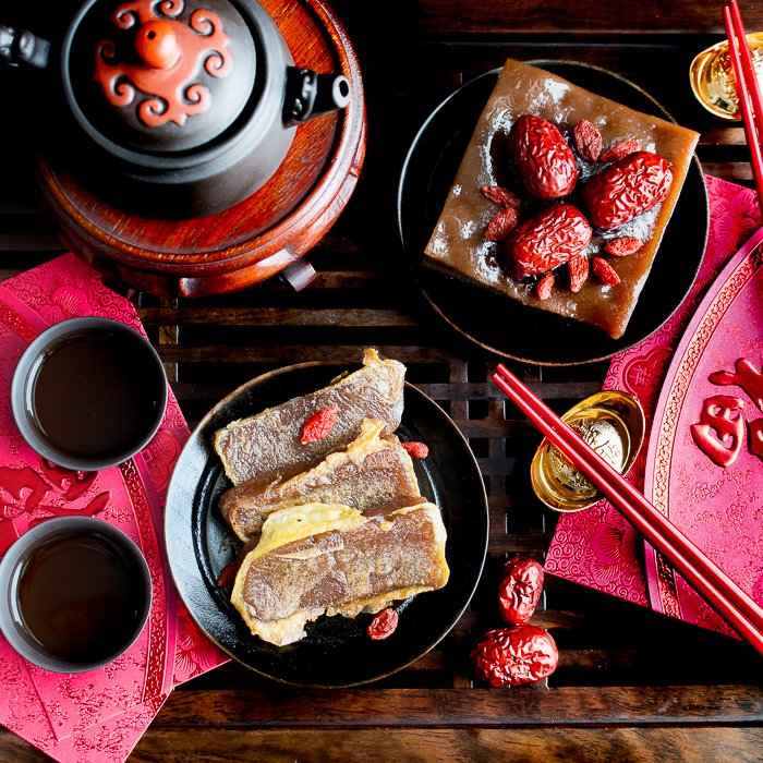 Nian gao that has been pan fried in egg sliced and on a black plate with a Chinese tea pot and tea.