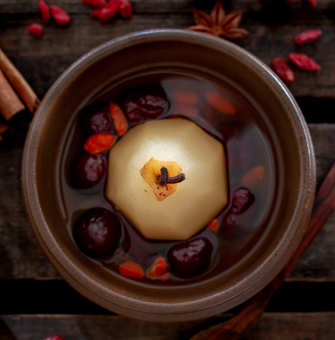 Chinese sweet pear dessert soup in a brown bowl garnished with red dates and goji berries.