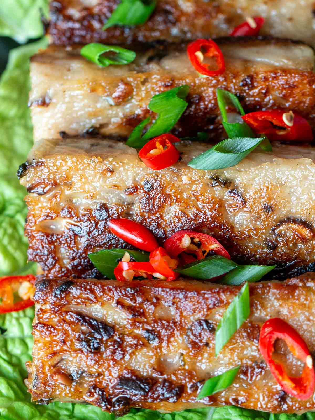 Pan fried Vegan Chinese Radish Cake on a plate lined with lettuce and garnished with chilis and green onions.