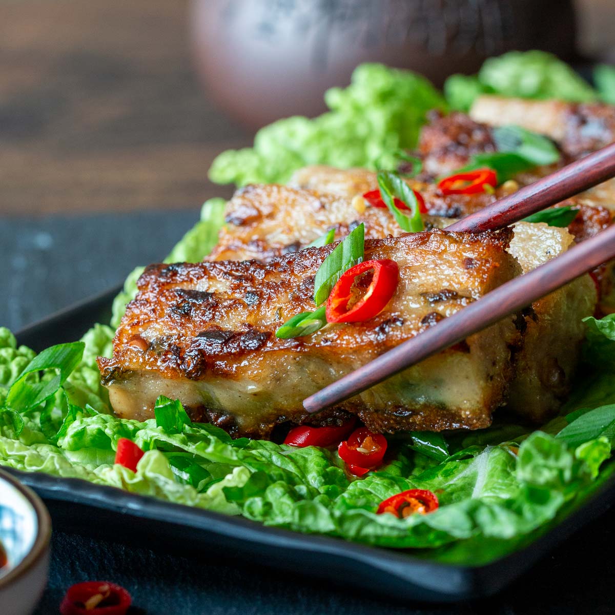 Vegan Chinese Radish cake on a bed of greens getting picked up with chopsticks.