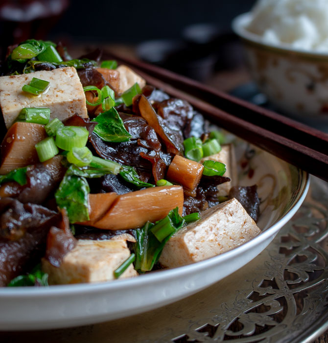 Wood ear mushroom and tofu stir fry with chop sticks on a Chinese green and white plate.