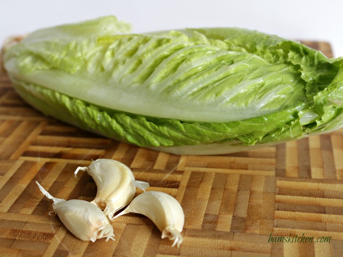 Head od romaine lettuce and garlic on a bamboo cutting board. 