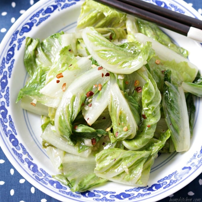 Top down shot of the stir fried lettuce in a blue and white plate with chopsticks.